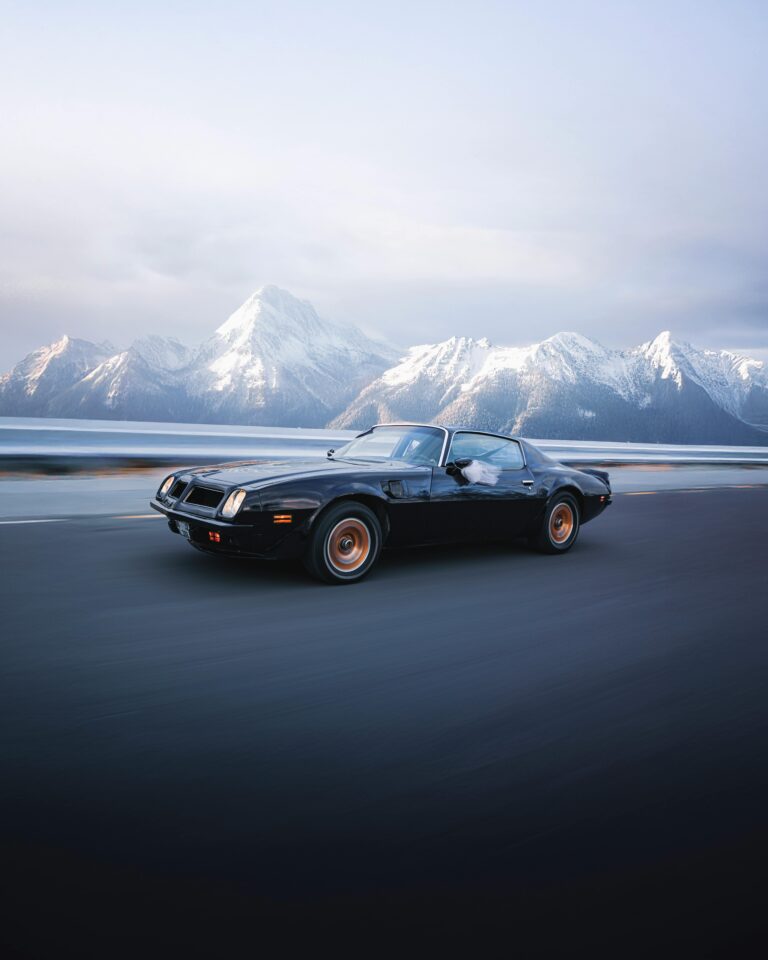 A vintage sports car speeds along a road with stunning snowy mountains in the background, exuding adventure